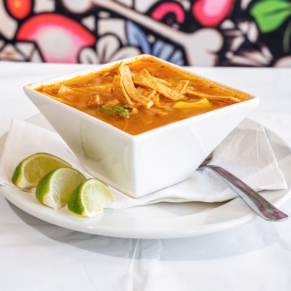 Tortilla soup in a white square bowl, garnished with tortilla strips and lime wedges.