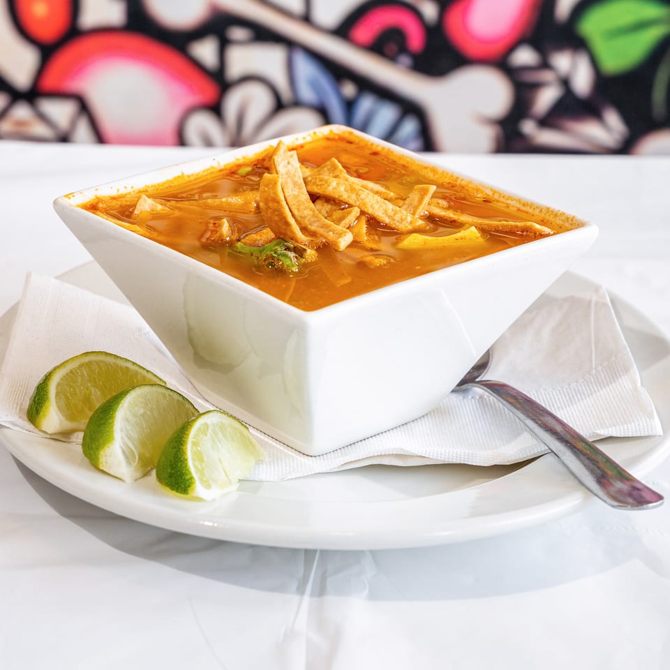 Tortilla soup in a white square bowl, garnished with tortilla strips and lime wedges.