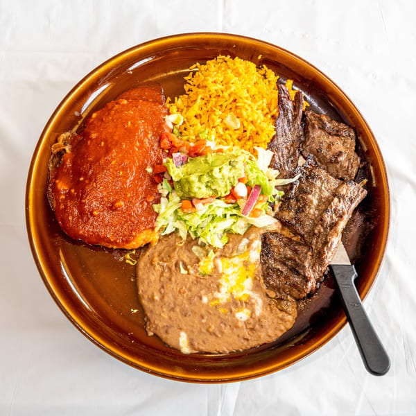 Large brown plate with grilled steak, yellow rice, refried beans, red sauce dish, and guacamole salad.
