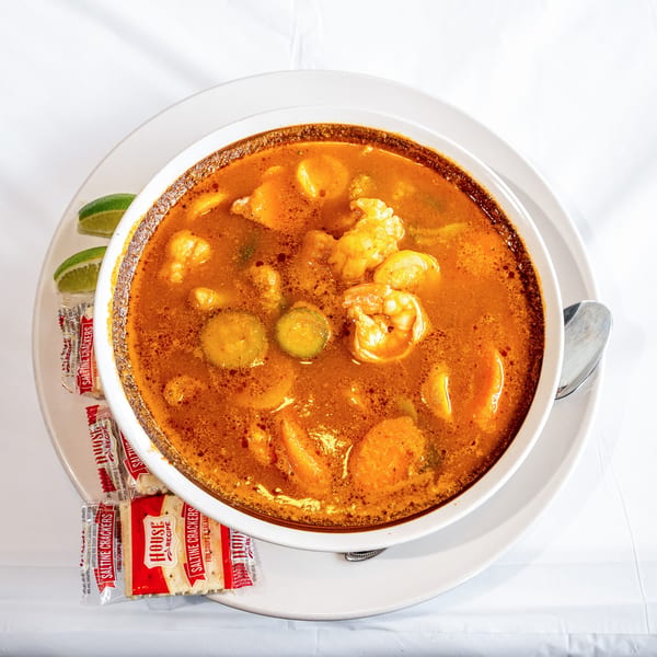 Vibrant orange seafood soup with shrimp, vegetables, lime, and saltine crackers.
