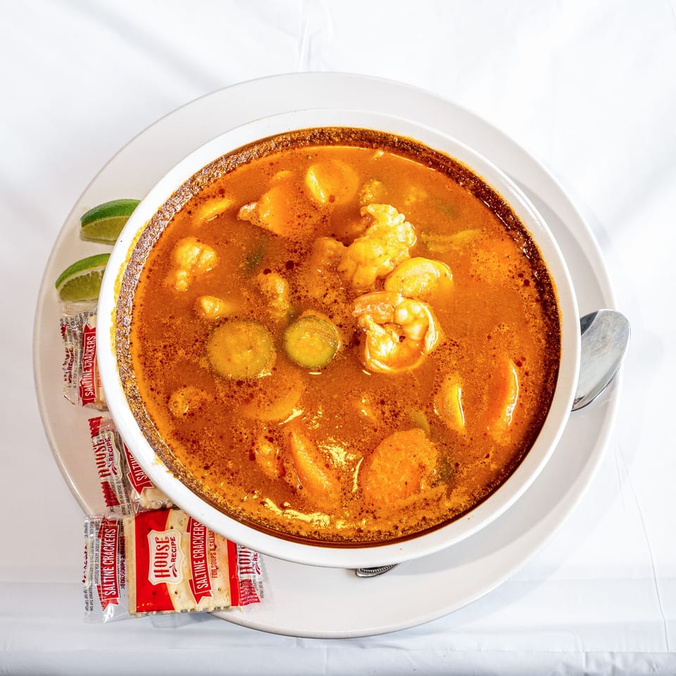 Vibrant orange seafood soup with shrimp, vegetables, lime, and saltine crackers.
