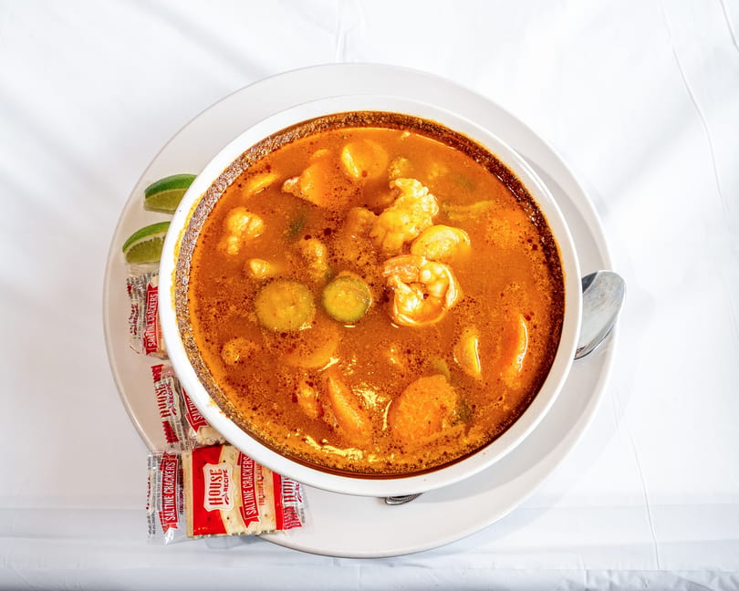 Vibrant orange seafood soup with shrimp, vegetables, lime, and saltine crackers.