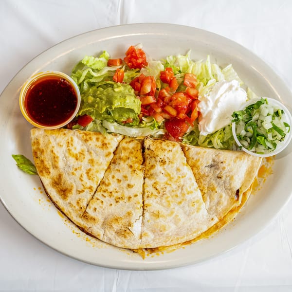 Quesadilla wedges with shredded lettuce, guacamole, diced tomatoes, sour cream, onions, and red sauce on a white plate.
