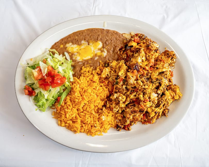 Mexican breakfast plate with scrambled eggs, refried beans, rice, and a side salad.