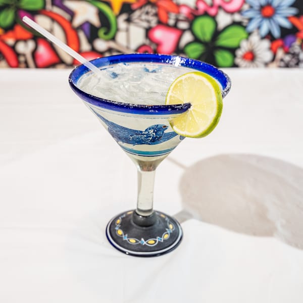 Iced margarita in a blue and white patterned glass with a lime and salted rim.