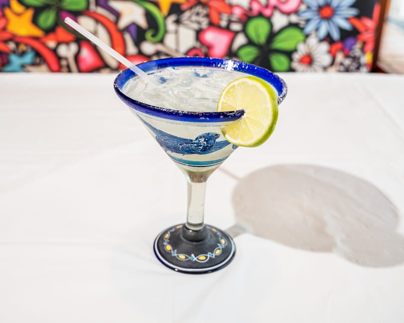 Iced margarita in a blue and white patterned glass with a lime and salted rim.
