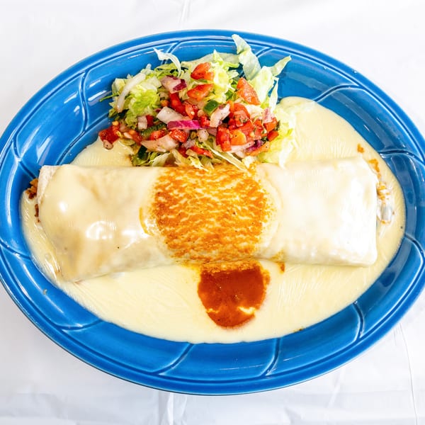 Large burrito smothered in white cheese sauce, with pico de gallo and lettuce on a blue plate.