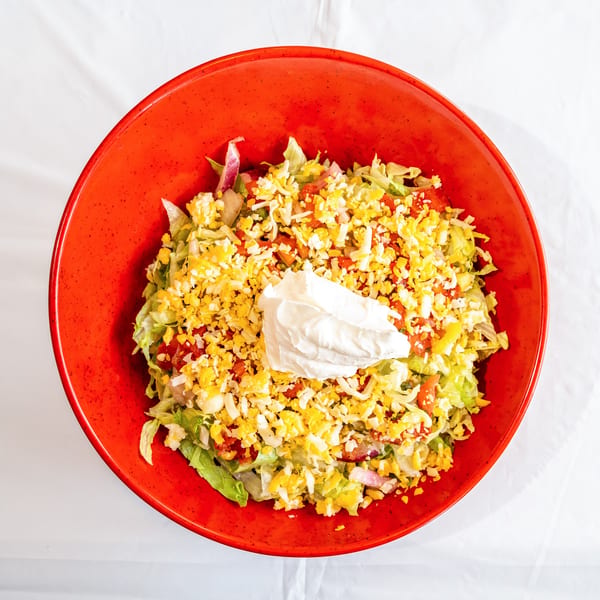 Colorful salad with lettuce, tomatoes, shredded cheese, and sour cream in a red bowl.