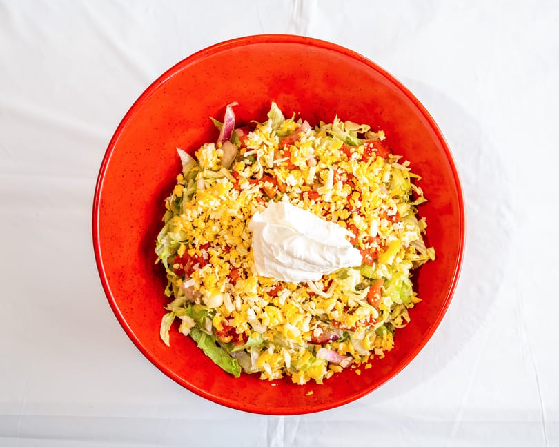 Colorful salad with lettuce, tomatoes, shredded cheese, and sour cream in a red bowl.